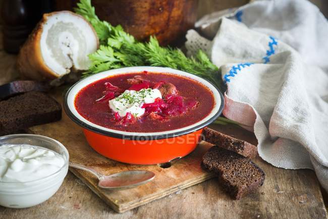 Traditional Russian and Ukrainian soup from beetroot called Borscht in red bowl over wooden desk with spoon — Stock Photo