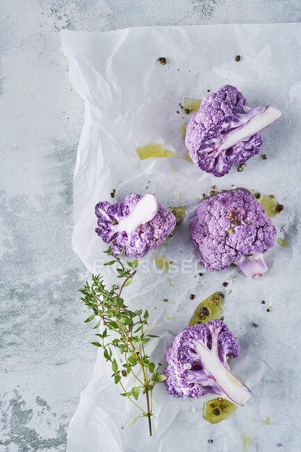 Coliflor púrpura con tomillo y aceite de oliva sobre papel de hornear - foto de stock