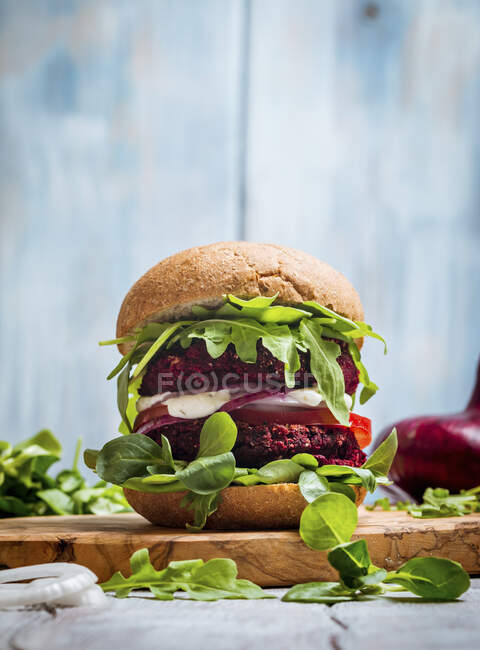 Вегетаріанський бургер з буряка, помідорів, кукурудзяного салату та руколи на дерев'яному фоні — стокове фото