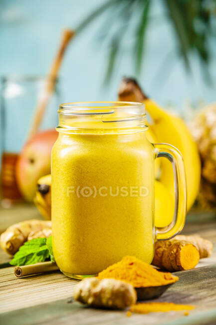 Batido de frutas amarillas con cúrcuma e ingredientes sobre una mesa - foto de stock
