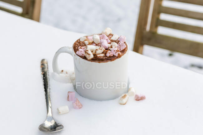 Чашка горячего шоколада с зефиром на столе в снегу — стоковое фото