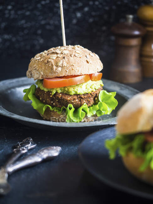Sanduíche de hambúrguer saudável de quinoa vegana e feijão vermelho com guacamole, alface fresca e tomate, servido em um pão de grão inteiro — Fotografia de Stock