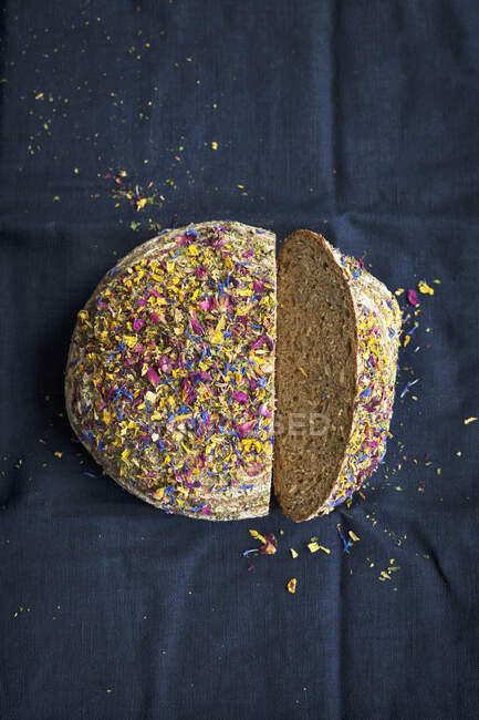 Hogaza de pan integral rematada con flores secas comestibles, en rodajas - foto de stock