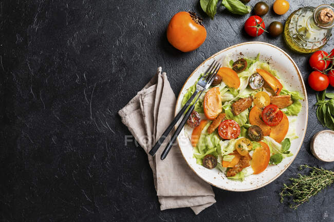 Frischer Salat mit Kaki, Huhn und Gemüse auf schwarzem Hintergrund — Stockfoto