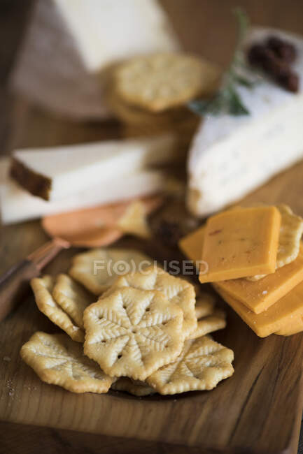 Galletas saladas y varios tipos de queso sobre tabla de madera - foto de stock