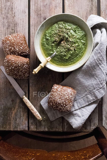 Spinach pesto in a bowl with bread at a wooden table and a chair — Stock Photo