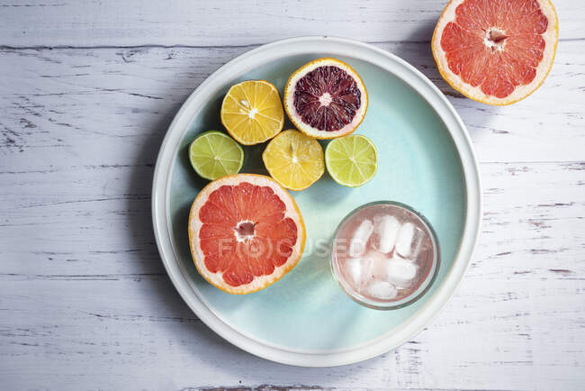 Halved citrus fruit, glass of grapefruit infused water with ice on blue plate — Stock Photo