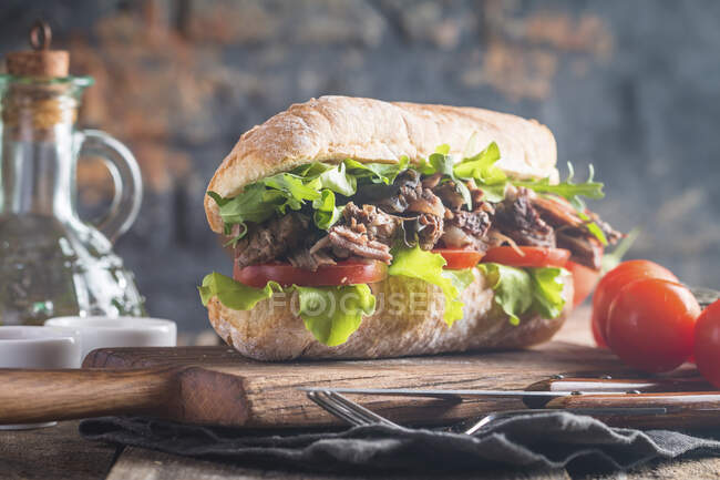 Сэндвич с говядиной с помидорами и салатом на деревянной доске с ингредиентами — стоковое фото