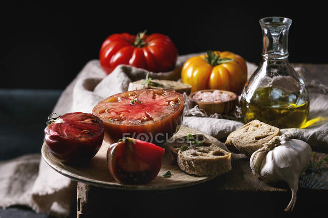 Tomates ecológicos rojos y amarillos con aceite de oliva, ajo, sal y pan para ensalada o bruschetta - foto de stock