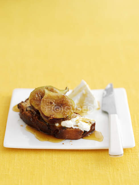Ломтик хлеба с медом, инжиром и сыром рикотта с ножом на тарелке — стоковое фото