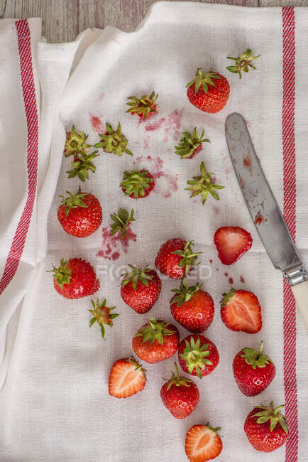 Fresh strawberries and green stems on cloth with knife — Stock Photo