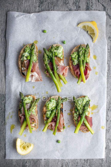 Slices of grilled ciabatta with crushed peas, ham and asparagus — Stock Photo
