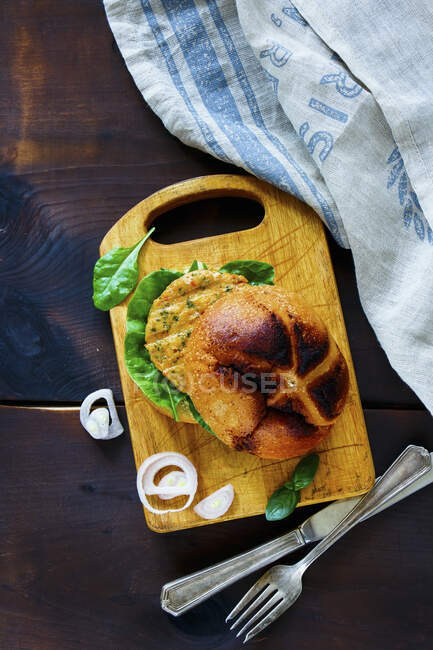 Top view of fresh fish and crab burger with sliced onion on little wooden cutting board over dark rustic background — Stock Photo