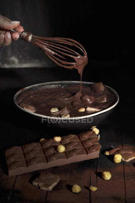 Main de femme avec fouet mélangeant chocolat fondu et cacahuètes dans un bol — Photo de stock