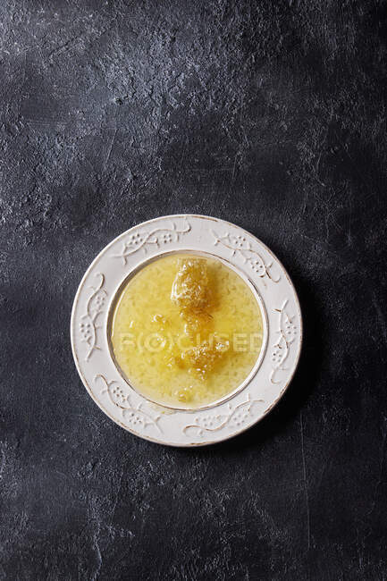 Honeycombs in liquid honey on white vintage plate over black texture background — Stock Photo