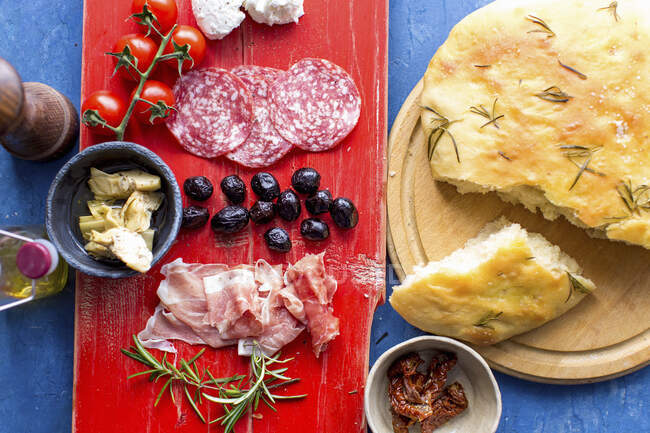 Antipasti: Focaccia mit Rosmarin, Fenchelsalami, Tomaten, Artischocken, schwarzen Oliven und Schinken — Stockfoto