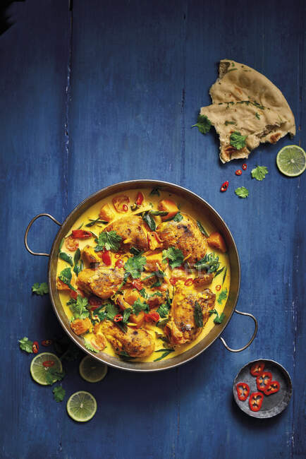 Curry de pollo asado estilo Keralan servido con pan de naan y cubierto con chile fresco y cilantro - foto de stock