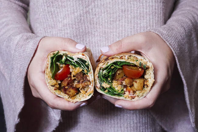 A woman holding a burrito with fried, diced potatoes, tomatoes, cream cheese, cheddar and spinach — Stock Photo
