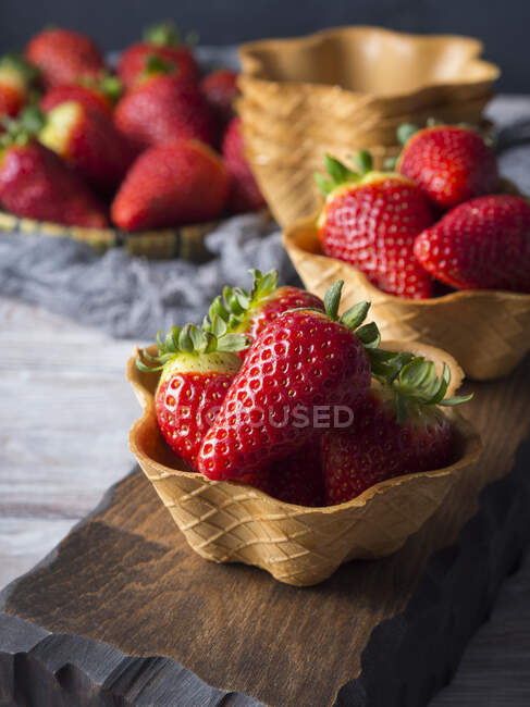 Strawberries in waffle cups on wooden surface — Stock Photo