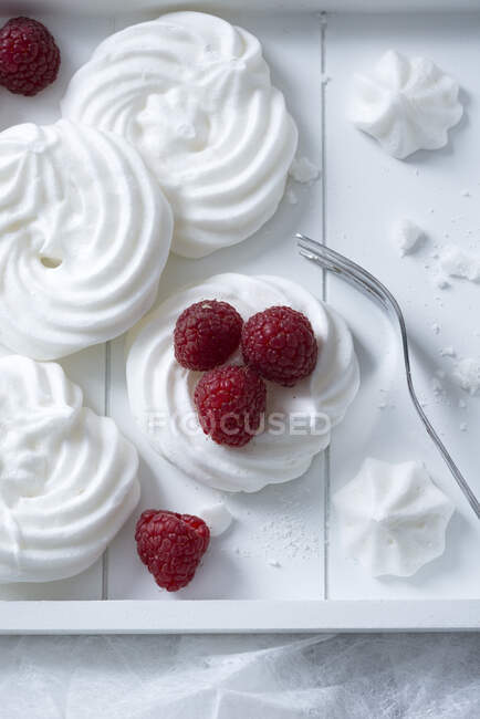 Meringues with fresh raspberries on white wooden tray — Stock Photo