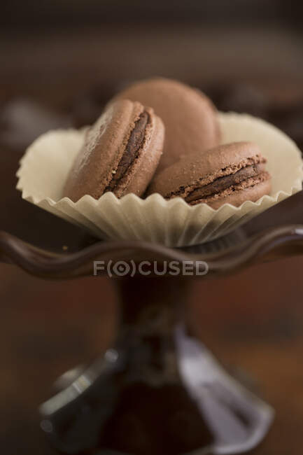 Chocolate macarons in paper cup on glass stand — Stock Photo
