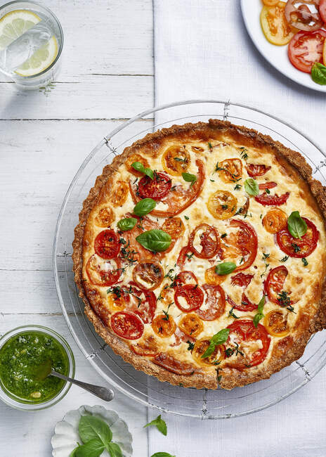 Mature cheddar and mixed heritage tomato tart with wholemeal crust served with pesto and topped with fresh basil leaves — Stock Photo