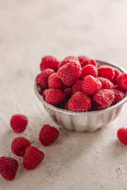 Fresh raspberries in metal bowl and on table — Stock Photo
