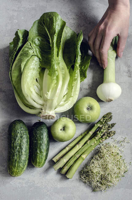 Зелені овочі та яблука, рука тримає цибулю — стокове фото