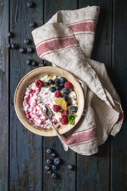 Ceramic bowl of homemade cottage cheese with blueberries, raspberries and honeycombs on kitchen towel over dark wooden plank background — Stock Photo