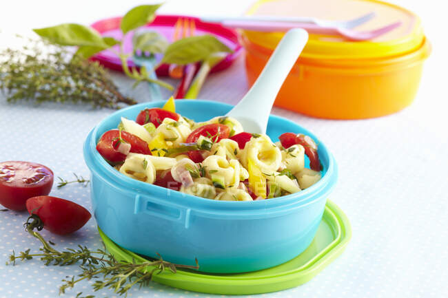 Colourful tortellini salad in Tupperware bowl with tomatoes and fresh herbs — Stock Photo