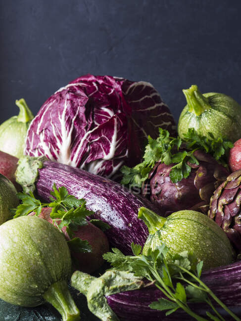 Assortment of raw green and purple vegetables - chicory, red potatoes, zucchini, artichokes and aubergines - on black background — Stock Photo