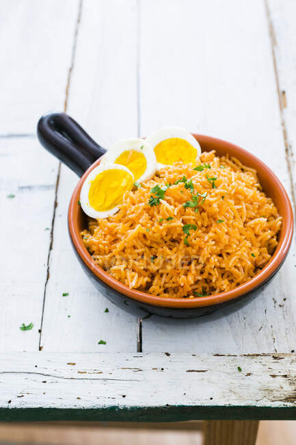 Terracotta bowl containing mexican red tomato rice garnished with hard boiled eggs and cilantro — Stock Photo