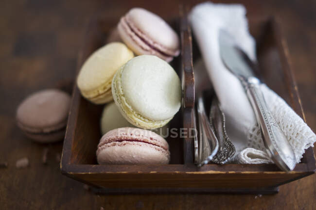 Verschiedene bunte Macarons mit Besteck und Servietten in Holzkiste — Stockfoto