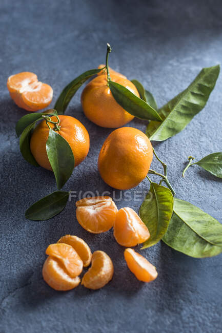 Целые и очищенные мандарины на каменной поверхности — стоковое фото