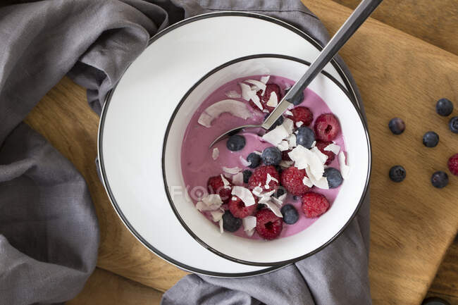 Yoghurt with acai powder topped with raspberries, blueberries and coconut chips — Stock Photo