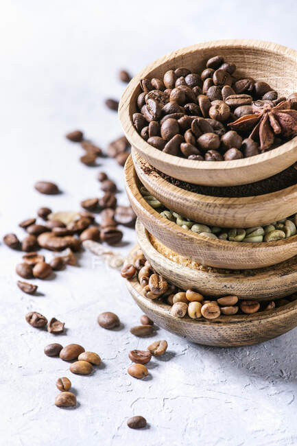 Variety of different coffee beans and spices in wooden bowls in stack over grey table — Stock Photo