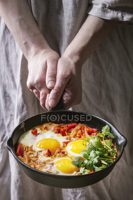 Традиційна ізраїльська кухня страва Шакшука (смажене яйце з овочевими помідорами і паприкою в чавунній сковороді в жіночих руках.) — стокове фото