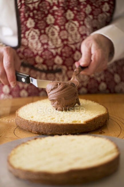 Un pastel que se hace: crema de chocolate que se extiende sobre un pastel partido a la mitad - foto de stock