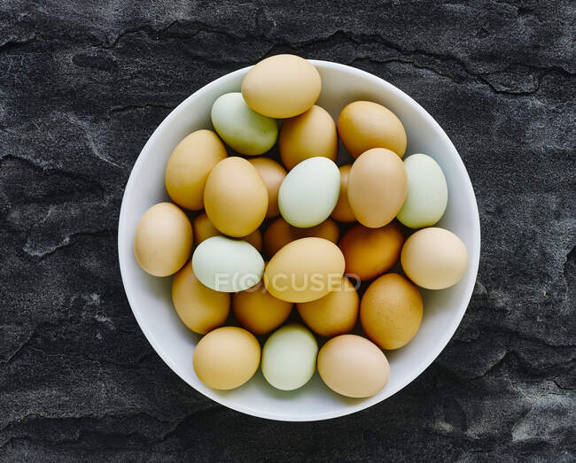 Différents oeufs frais colorés dans un bol blanc — Photo de stock