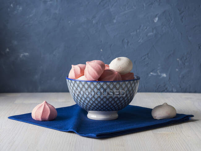 Meringues roses et blanches dans un bol bleu et sur une serviette en tissu — Photo de stock