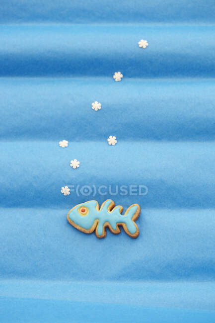 Fish shaped biscuit with blue icing against a blue background — Stock Photo