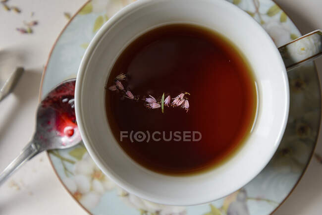 A cup of black tea with herbs, a spoon with red jam — Stock Photo
