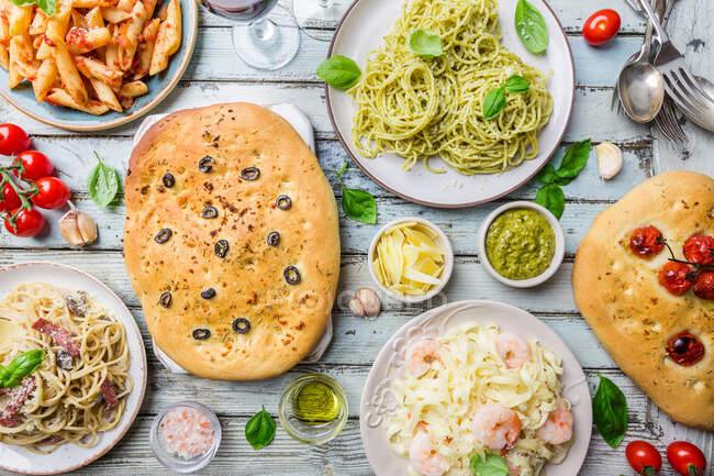 Італійський стіл з декількома тарілками макаронів з різним соусом і квітковим хлібом. — стокове фото
