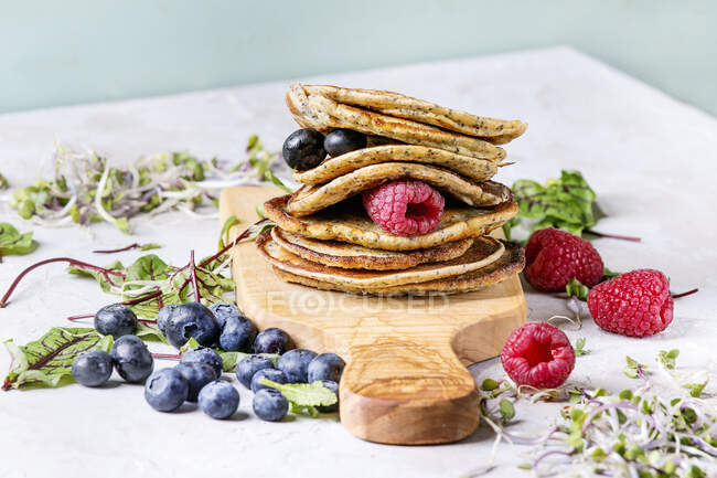 Stack of vegan chickpea pancakes on olive wood cutting board with green salad, sprouts, berries, over grey kitchen table — Stock Photo