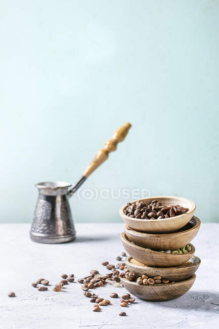 Varietà di diversi chicchi di caffè e spezie in ciotole di legno in pila sopra tavolo grigio — Foto stock