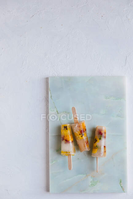 Water icecreams with elderflower syrup and eatable flowers on a marble plank and a white backdrop — Stock Photo