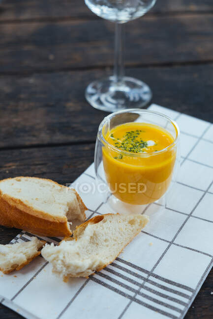 Un vaso de sopa de calabaza junto a un pedazo de pan blanco - foto de stock