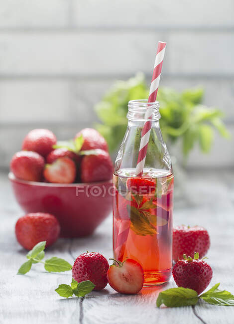 Bebida refrescante de verão com morango em uma garrafa de vidro na mesa de madeira branca — Fotografia de Stock