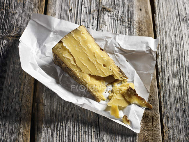 A slice of alpine cheese on a weathered wooden board — Stock Photo