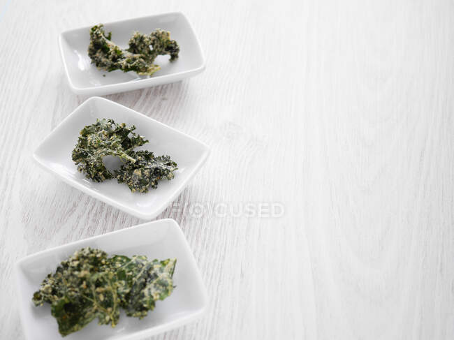 Kale chips in white bowls on a wooden board — Stock Photo